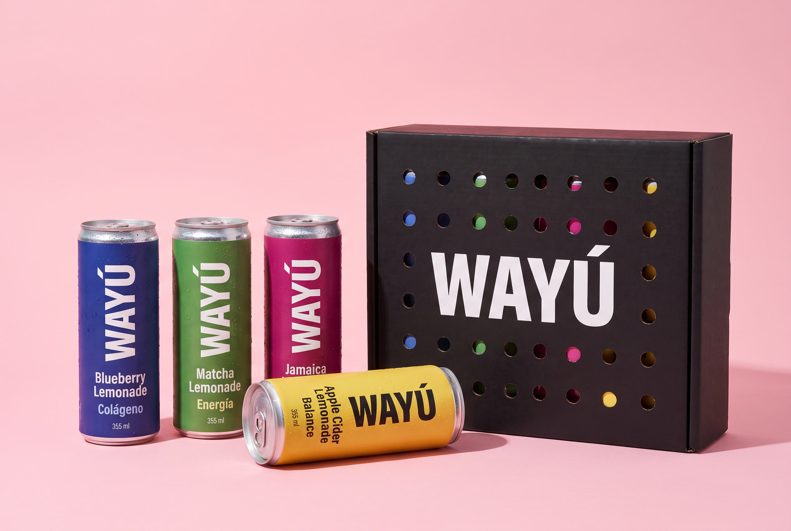 Latas Wayú de Blueberry, Matcha, Jamaica y Apple Cider Lemonade junto a la caja negra Wayú sobre fondo rosa