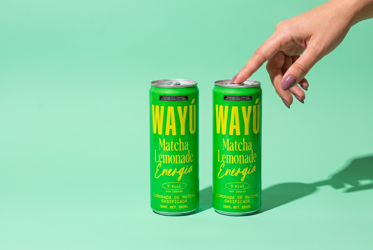Wayú Matcha Lemonade Energía: dos latas de limonada gasificada de matcha, 3 kcal, con mano tocando la lata sobre fondo verde menta